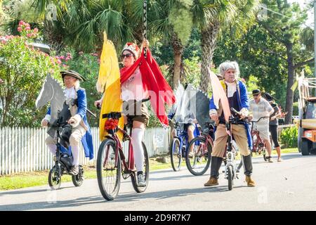 In Kostümen gekleidet fahren Radfahrer während der jährlichen Parade zum Unabhängigkeitstag am 4. Juli 2019 in Sullivan's Island, South Carolina, die Straße hinunter. Die winzige wohlhabende Sea Island Beach Gemeinschaft gegenüber von Charleston veranstaltet eine übergroße Golfwagen Parade mit mehr als 75 dekorierten Karren. Stockfoto