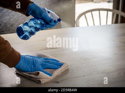 Oberflächenreinigung Spritzen antibakterielle Desinfektionsflüssigkeit mit Flasche Waschtisch zu Hause. Mann mit Handschuhen und Handtuch während der Frühjahrsputz. Stockfoto