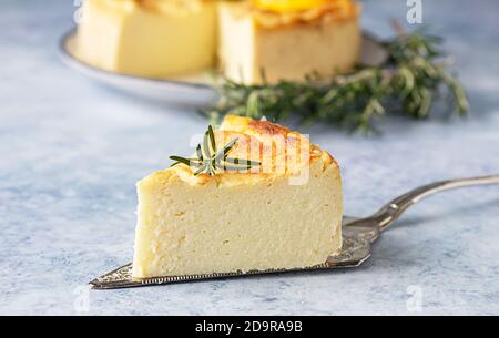 Käsekuchen mit Zitronenvanille, verziert mit Rosmarin-, Minze- und Zitronenscheiben. Ricotta keine Kruste Käsekuchen oder Kasserolle. Blauer Betonhintergrund. Stockfoto