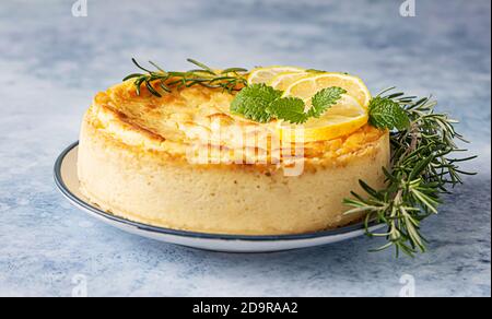 Käsekuchen mit Zitronenvanille, verziert mit Rosmarin-, Minze- und Zitronenscheiben. Ricotta keine Kruste Käsekuchen oder Kasserolle. Blauer Betonhintergrund. Stockfoto