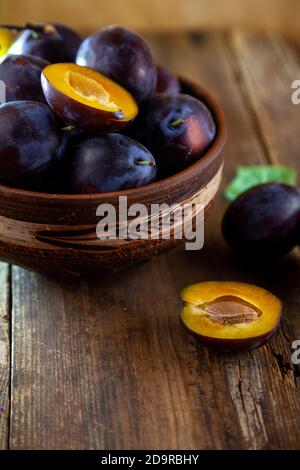 Blaue Pflaume in einer Schüssel auf einem Holztisch. Pflaumen in einem Schnitt. Draufsicht, für Text platzieren. Obsthintergrund mit Kopierraum. Stillleben Essen. Stockfoto