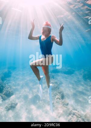 Weihnachtsferien Party mit Freitaucher. Happy Freediver Frau mit Neujahr Mütze gleitet unter Wasser mit Flossen in blauen Ozean. Stockfoto