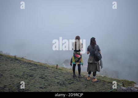 Zwei junge Besucherinnen warten im Nebel auf den Sonnenaufgang in den Ruinen von Machu Picchu, Peru Stockfoto