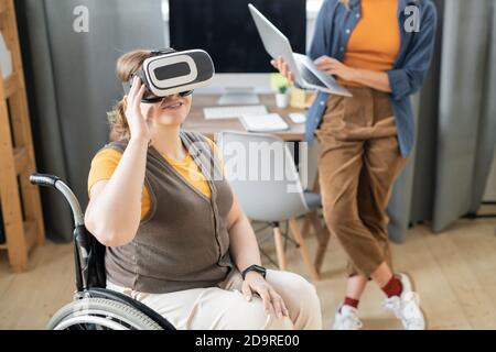 Deaktivieren Sie Geschäftsfrau in vr Headset sitzen im Rollstuhl gegen beschäftigt Kollege Stockfoto