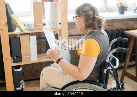 Junge deaktivieren weibliche Buchhalterin im Rollstuhl Blick durch Finanzpapiere Stockfoto