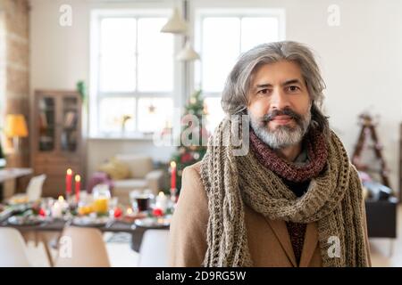 Reifer bärtiger Mann im Mantel und gestrickter Schal stehen dagegen Festlicher Tisch Stockfoto