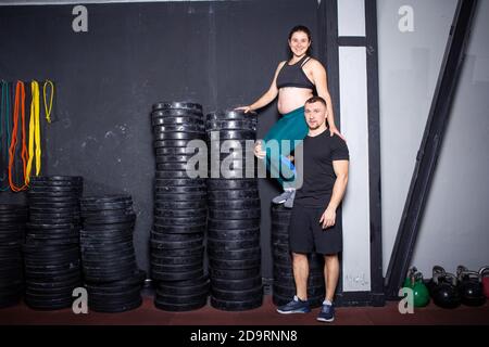 Workouts und Übungen für schwangere Frauen im Fitnessstudio. Kaukasische Athleten Bodybuilder, Ehepaar Ehemann und Ehefrau genießen Schwangerschaft und posieren nach Stockfoto