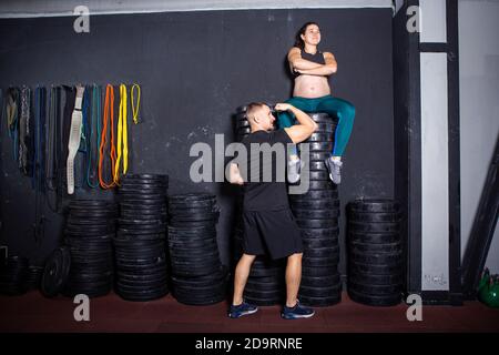 Schwangerschaftszeit bei sportlich starken muskulösen Frauen. Gemeinsame Workouts und Übungen des Paares während der Schwangerschaft in der Turnhalle. Mann und schwangere Frau Stockfoto