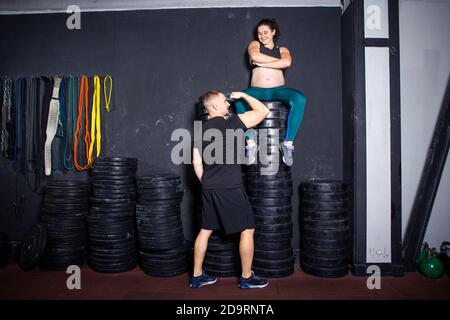 Workouts und Übungen für schwangere Frauen im Fitnessstudio. Kaukasische Athleten Bodybuilder, Ehepaar Ehemann und Ehefrau genießen Schwangerschaft und posieren nach Stockfoto