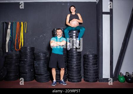 Workouts und Übungen für schwangere Frauen im Fitnessstudio. Kaukasische Athleten Bodybuilder, Ehepaar Ehemann und Ehefrau genießen Schwangerschaft und posieren nach Stockfoto