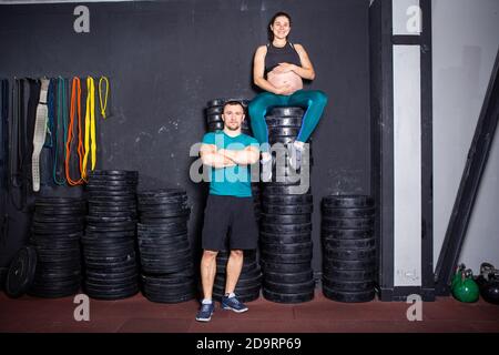 Schwangerschaftszeit bei sportlich starken muskulösen Frauen. Gemeinsame Workouts und Übungen des Paares während der Schwangerschaft in der Turnhalle. Mann und schwangere Frau Stockfoto