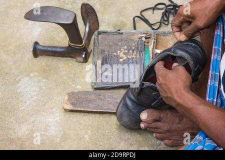 Indische lokale Schuster Reparatur Schuhe neben der Straße von Hand mit Werkzeugen in traditioneller Weise. Natürliche Schuss Darstellung der täglichen Arbeit eines regelmäßigen Schuster. Stockfoto
