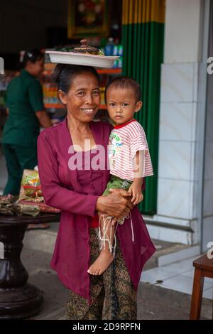 Bali, Indinesien - 11. MÄRZ 2013: Frau mit Kind in den Armen geht in einem Geschäft einkaufen Stockfoto