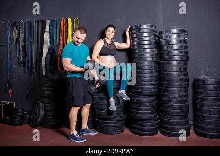 Workouts und Übungen für schwangere Frauen im Fitnessstudio. Kaukasische Athleten Bodybuilder, Ehepaar Ehemann und Ehefrau genießen Schwangerschaft und posieren nach Stockfoto