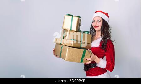 Weihnachtseinkäufe Frau hält viele Weihnachtsgeschenke in ihren Armen trägt weihnachtsmütze. Schöne junge weibliche Modell auf grauem Hintergrund. Mädchen gekleidet als Stockfoto