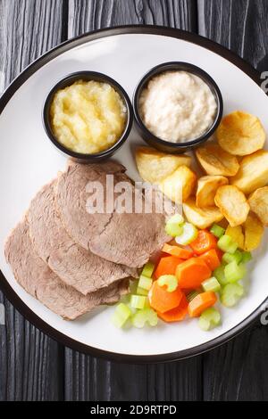 Typisch österreichischer Tafelspitz gekocht mit Rindfleisch, frischem Gemüse, aromatischer Würze serviert mit Kartoffeln, Meerrettich und Apfelsauce close-up in einem pla Stockfoto