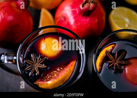 Blick von oben auf die zwei Glas Becher mit Glühwein auf braunem Holz- Hintergrund mit weichen Fokus auf Granatapfel. Auf der Oberseite der Rebe Oberfläche Sternanis und Scheibe Stockfoto