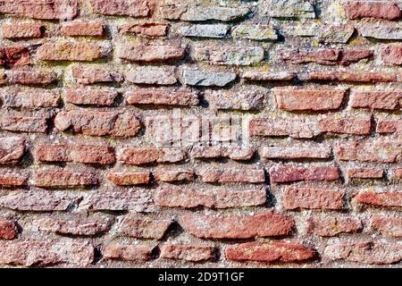 Nahaufnahme einer Sandsteinwand, die Struktur besteht aus schmalen Platten verschiedener Arten von rotem Sandstein in einem halbregelmäßigen Muster. Stockfoto