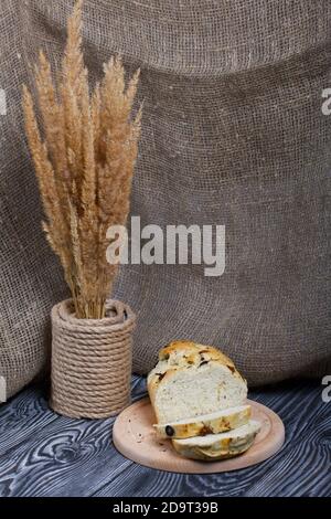 Focaccia Brot mit Oliven und getrockneten Tomaten. In der Nähe ist ein Strauß getrocknetes Gras. Auf Kiefernbrettern. Stockfoto