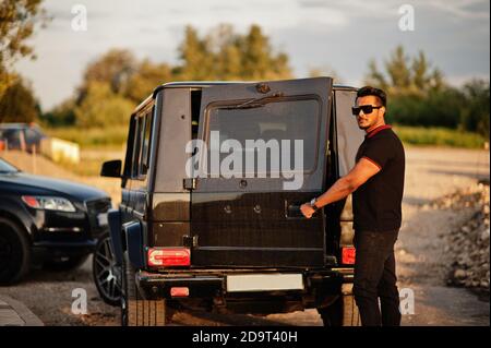 Asian Mann tragen auf ganz schwarz posiert in der Nähe suv-Auto, öffnen Hintertür. Stockfoto