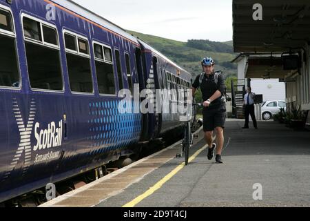 Girvan Railway Station, South Ayrshire, Schottland, Großbritannien. Ein Radfahrer mit Shorts und Schutzhelm kommt mit dem Zug am Bahnhof Girvan an, bevor er eine Radtour startet Stockfoto