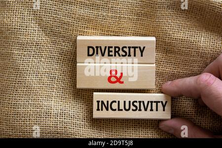 Holzblöcke bilden die Worte "Vielfalt und Inklusivität" auf Leinwand Hintergrund. Männliche Hand. Business, Diversity und Inklusivitätskonzept. Stockfoto