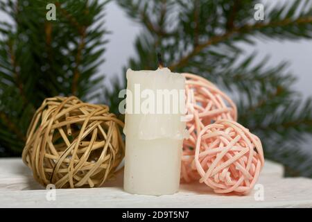 Kerze auf weißen Kiefernbrettern. In der Nähe sind Rattanbälle. Vor dem Hintergrund von Tannenzweigen. Stockfoto