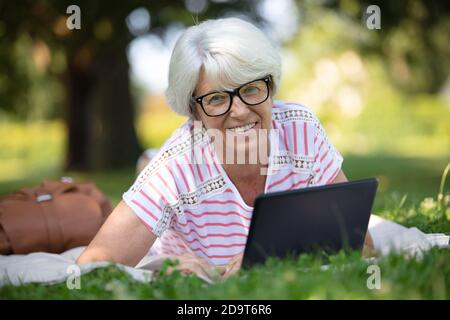 Reife Frau auf Gras liegend mit Computer Stockfoto