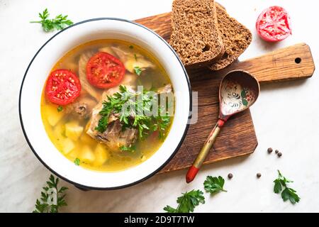 Fischsuppe mit Karpfen, Kartoffeln, Petersilie, Tomaten in Emaille-Schüssel steht auf einem Brett Stockfoto