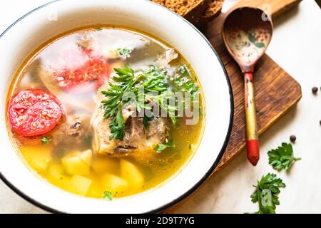 Fischsuppe mit Karpfen, Kartoffeln, Petersilie, Tomaten in Emaille-Schüssel steht auf einem Brett Stockfoto