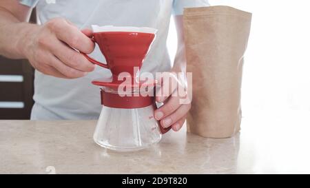 Stellen Sie das V60 neben dem Kaffeepaket auf dem Tisch ein. Männer Hand hält Glas Server. Pourover Stockfoto