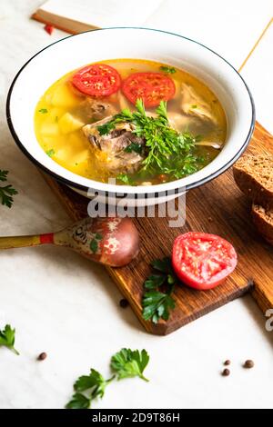 Fischsuppe mit Karpfen, Kartoffeln, Petersilie, Tomaten in Emaille-Schüssel steht auf einem Brett Stockfoto