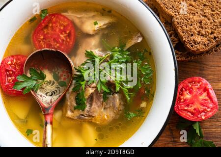Fischsuppe mit Karpfen, Kartoffeln, Petersilie, Tomaten in Emaille-Schüssel steht auf einem Brett Stockfoto
