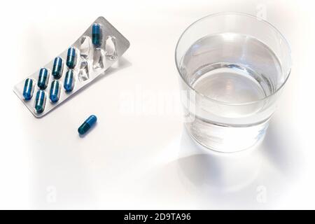 Blisterpackung mit blauen Pillen und einem Glas Wasser Auf weißem Hintergrund Stockfoto