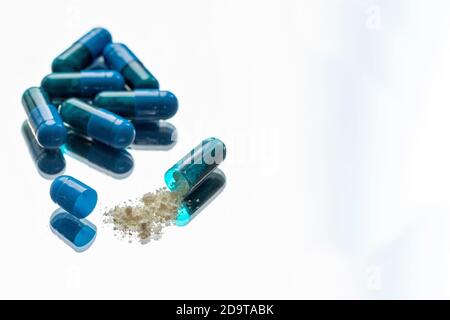 Blaue Pillen im Vordergrund mit einer von ihnen geöffnet Mit der Medizin auf weißem Hintergrund Stockfoto