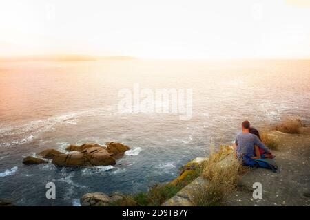 Verliebte Paare, die den Sonnenuntergang auf einer Klippe mit beobachten Das Meer des Hintergrundes Stockfoto
