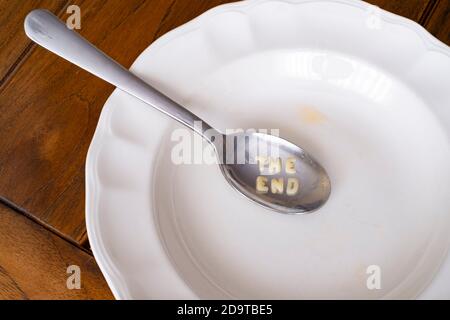 Leere Alphabet Suppenteller mit der Nachricht des Endes in einem Löffel auf einem weißen Teller auf einem Holztisch, Draufsicht Stockfoto