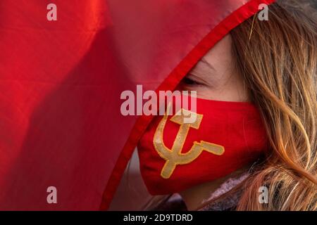 Moskau, Russland. 7. November 2020 AUF dem Maneschnaja-Platz wird EINE Frau mit Gesichtsmaske und einem Symbol für die Arbeit in der Sowjetunion während einer Prozession gesehen, die von Kommunisten Russlands anlässlich des 103. Jahrestages der bolschewistischen Revolution vom 1917. Oktober auf dem Roten Platz im Zentrum Moskaus, Russland, veranstaltet wurde Stockfoto