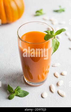 Frischer Kürbissaft in einem hohen Glas mit Minze verziert Blätter und Kürbiskerne schließen sich auf einem grauen Hintergrund an Stockfoto