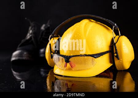 Nasse Arbeitskleidung für einen Produktionsarbeiter. Regentropfen auf Helm und Brille. Dunkler Hintergrund. Stockfoto