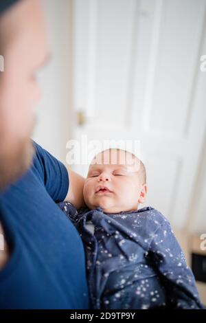 Baby Girl schläft in ihrem blauen Onesie, während Papa Bewundert Sie Stockfoto