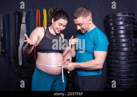 Junges Paar messen Mama Bauch. Schöne schwangere paar Messung Bauch. Der Mann misst die Größe des Bauches seiner schwangeren Frau mit einem Maßband Stockfoto