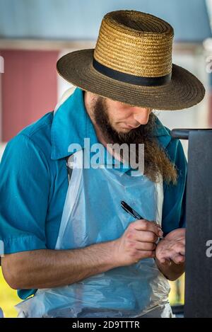 Amish, Lancaster County, Pennsylvania. Amish Mann in Strohhut berechnet den Gesamtverkaufspreis durch Schreiben auf seiner Handfläche, auf dem ländlichen Bauernhof Stand Stockfoto