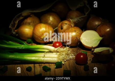 Frühlingszwiebeln und Zwiebeln in Beutel mit Kirschtomaten herum Auf Holzbrett Stockfoto