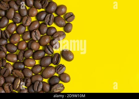 Schwarze Kaffeebohnen auf gelbem Hintergrund. Links vertikale Position Objekte, kopieren Platz für Text auf der rechten Seite. Nahaufnahme, flache Lay bunte Kaffee Stillleben. Stockfoto