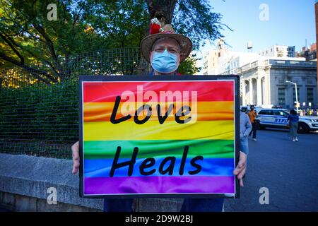 Ein Mann mit Gesichtsmaske hält ein Plakat, auf dem steht: Liebe heilt, wenn New York City ausbricht, um Bidens Sieg als 46. US-Präsident im Washington Square Park in New York zu feiern. Stockfoto
