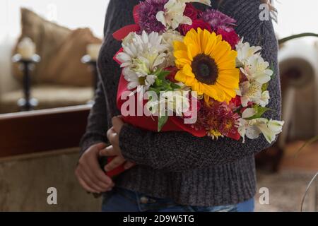 Die Person, die den schönen und bunten Blumenstrauß mit der Sonnenblume und verschiedenen Arten der Blumen, im Zimmer, das Geschenk der Liebe hält Stockfoto