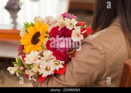 Person mit Jacke hält schöne Blumenstrauß mit Sonnenblume, Rosen und verschiedene Arten von Blumen, romantische Details, Natur Stockfoto