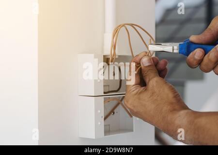 Elektriker verwenden einen Zangenschlüssel, um den Netzstecker an der Wand zu installieren. Stockfoto