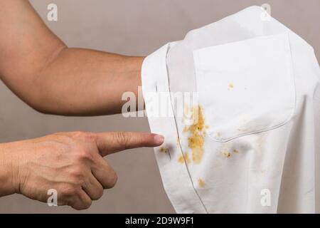 Person, die auf verschütteten Curryfleck auf weißem Hemd zeigt. Stockfoto